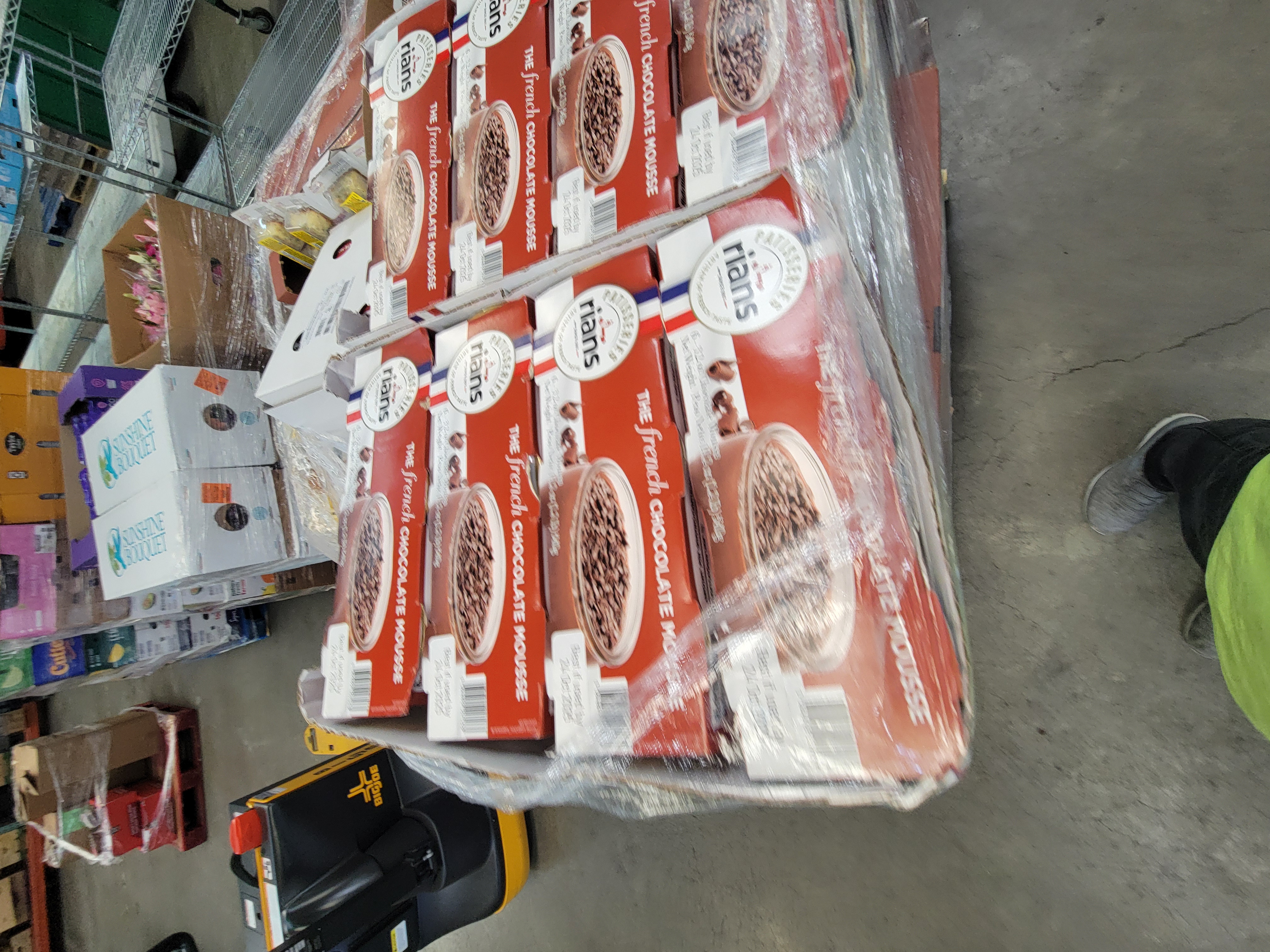 Boxes of french chocolate mousse with a pallet jack and boxes of assorted food behind it.